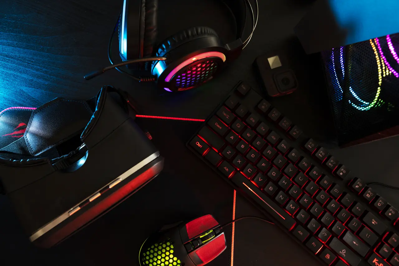Eine Nahaufnahme zeigt ein Set aus hochwertigem Gaming Zubehör: eine mechanische Tastatur, eine präzise Gaming-Maus und ein Over-Ear-Headset, beleuchtet in RGB-Farben.